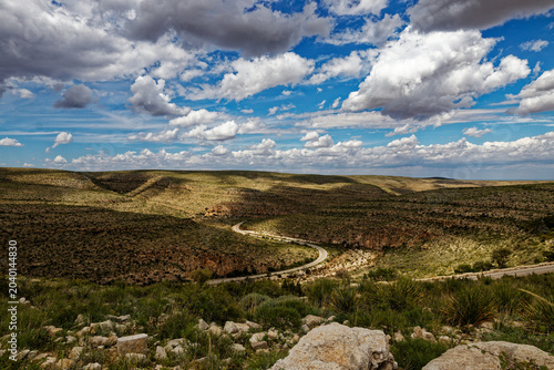 Winding Road through Sunny Desert Hills with Dramatic Clouds