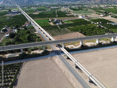 Aerial drone view of a modern high speed train railway bridge crossing the Tajo Segura water transfer pipeline surrounded by agricultural orchards at the Huerta de Orihuela in Spain