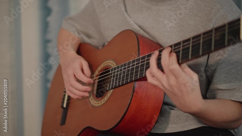 Young musician practicing guitar closeup, student practices chord patterns on nylon string acoustic instrument, fingers moving along frets, gentle strum and focused posture, quiet home lesson