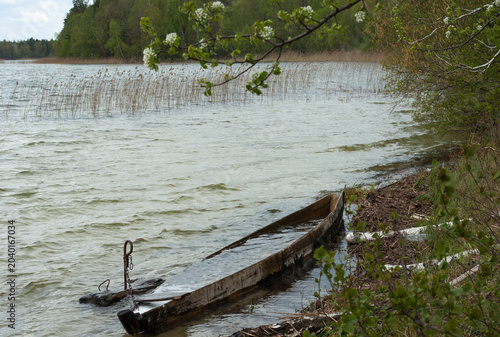 Old sunken wooden boat filled with water on the shore of a windy lake.