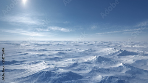 A vast expanse of snow covered terrain under a bright sun and a clear blue sky with faint clouds above
