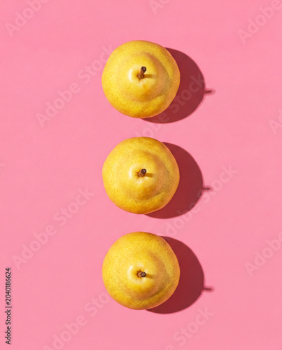 Minimalist image of three delicious pears arranged vertically on a pink background