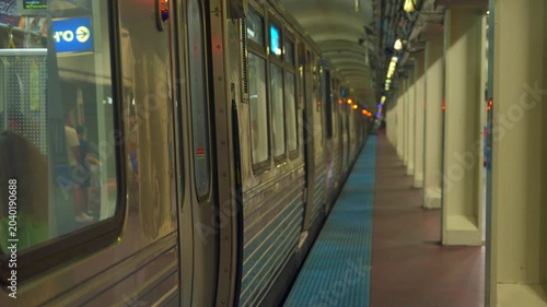 Chicago subway train standing at an underground platform with glowing lights and long perspective view. Urban public transportation scene showing rail cars, columns, and station architecture.