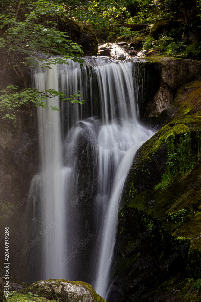 Obraz premium Triberger Wasserfälle im Schwarzwald mit sonnenbeschienenem, herabstürzendem Wasser und moosbewachsenen Felsen 