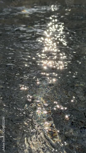 Slow motion handheld close up of sunlight reflections rippling across shallow shoreline beach at daytime summer