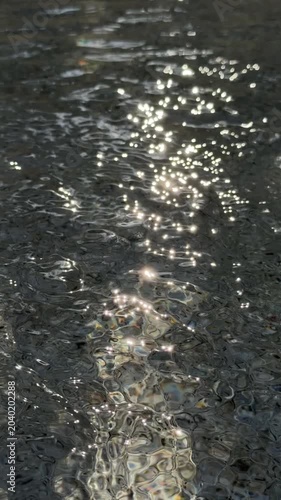 Slow motion close up handheld of sunlight sparkling on rippling water surface in shallow river near shore