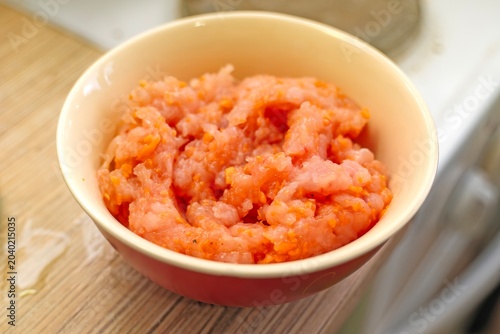 Small ceramic bowl filled with minced chicken, spices, and grated carrot, placed on a table
