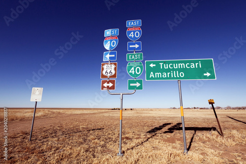 Historic Route 66 and interstate 40 highway road sign pointing towards Tucumcari and Amarillo against clear blue sky.