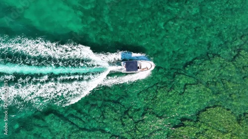 Aerial top down view of a speed boat cruising through sea waves. Drone shot of blue water and white foam trail. Summer vacation, travel and maritime leisure concept.