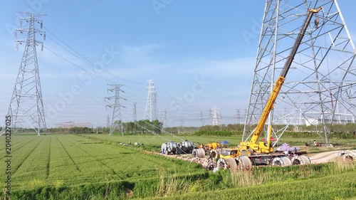 Construction scene with power line towers and workers under high voltage transmission lines in a green field