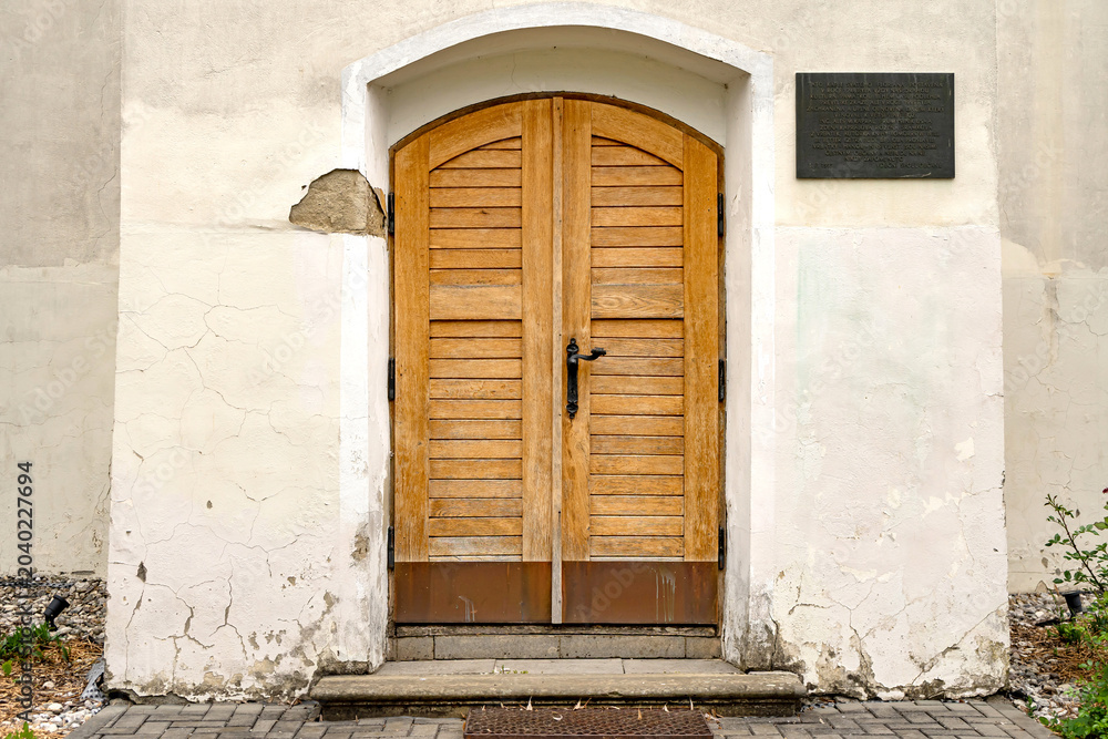 Fototapeta premium Old wooden church door with cracked historic facade in Czech village obec Vrbatky, Czech Republic - May 3, 2026