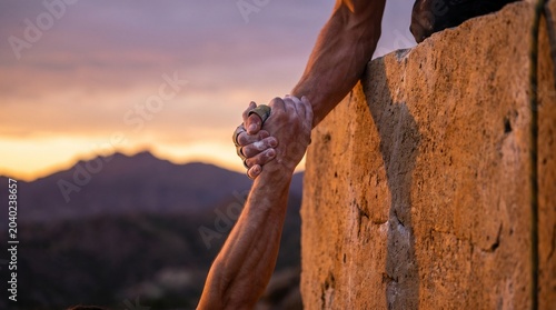 A person holds a rock climbing handhold at a scenic mountain location during sunset.