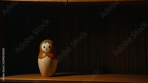 Minimalist wooden nesting doll on a shelf in a dark room with dramatic spotlighting.