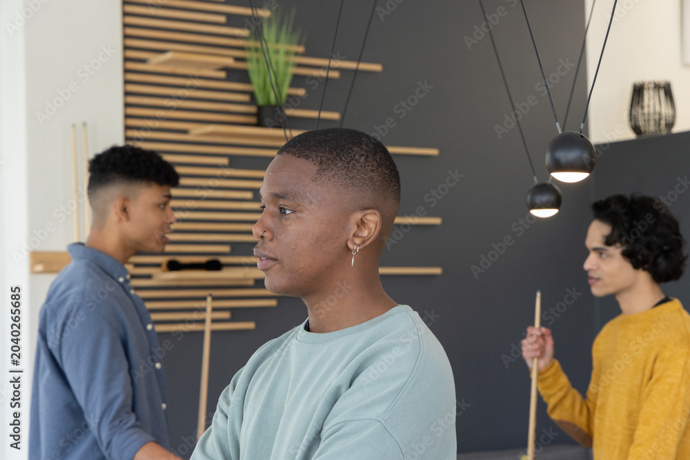 Naklejka premium Diverse male friends standing around pool table under pendant lights holding cues and watching