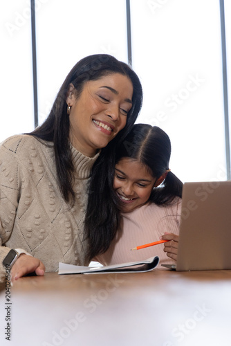 African American mother and Indian child sitting at table with laptop and notebook, smiling