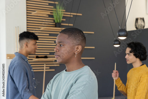 Diverse male friends standing around pool table under pendant lights holding cues and watching