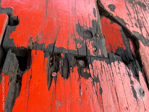Close-up of weathered red painted wood texture, showing deep cracks, peeled paint, and rusty nails embedded, perfect for rustic or grunge background