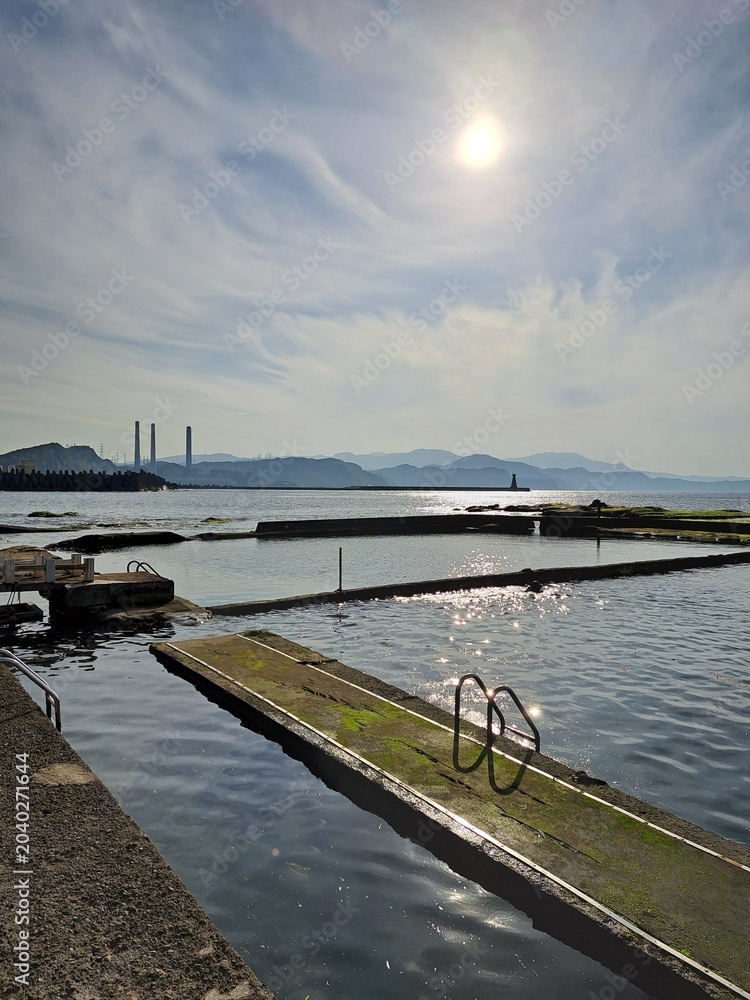 Fototapeta premium Coastal swimming pools with sun reflection and industrial background