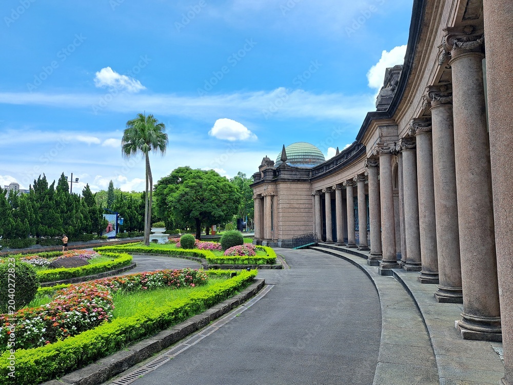 Fototapeta premium Curved stone colonnade with manicured flower gardens and palm tree