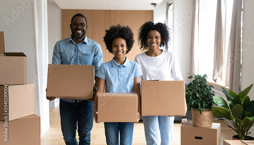 Smiling diverse family carrying moving boxes into their new home, symbolizing relocation and homeownership