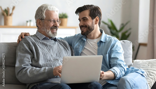 Smiling grandfather and grandson looking at a laptop screen together on a couch, sharing a moment of connection and learning
