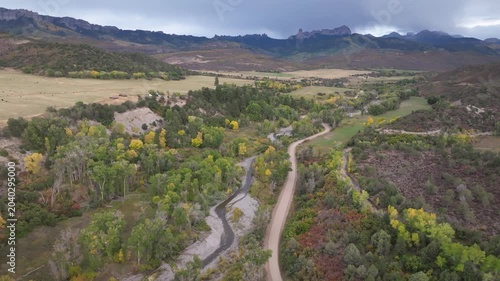 Aerial view of Colorado fall landscapes featuring fall foliage trees, rivers, and dirt road while capturing the beauty of Chimney Rock and Courthouse Mountain in the San Juan Mountain wilderness - 4K 