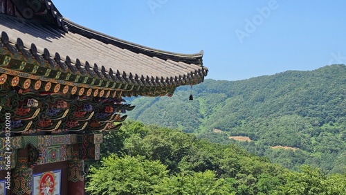 Foto Traditional Korean temple roof eaves with wind chime against green mountain and