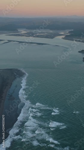 Aerial view of the coastline and harbour mouth at sunset in Kawhai, New Zealand. The water flows into the Tasman Sea, creating a scenic landscape.