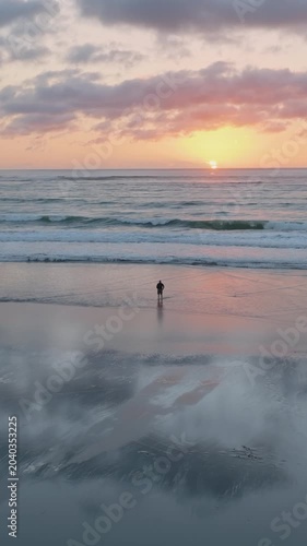 Sunset at Piha Beach, Auckland, New Zealand. People enjoy the reflections on the wet sand. A lone figure walks towards the ocean. Peaceful and serene.
