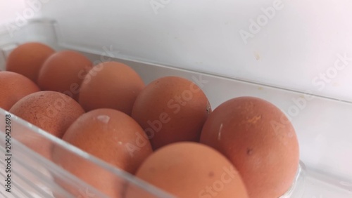 Brown eggs arranged in a clear container inside a refrigerator, showcasing the gradual shift in perspective and positioning across the frames