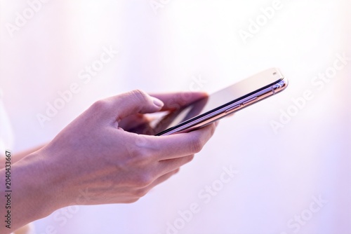 Hands Holding Rose Gold Smartphone Against Soft White Background