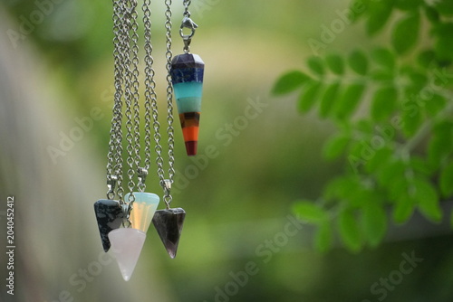 Several crystal pendulums, including a colorful chakra one, dangle beautifully near green leaves.