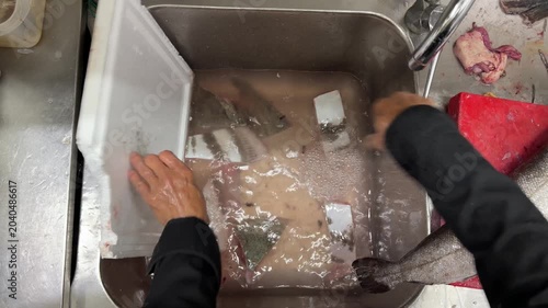Chef cleaning and gutting a large fish in a professional kitchen sink