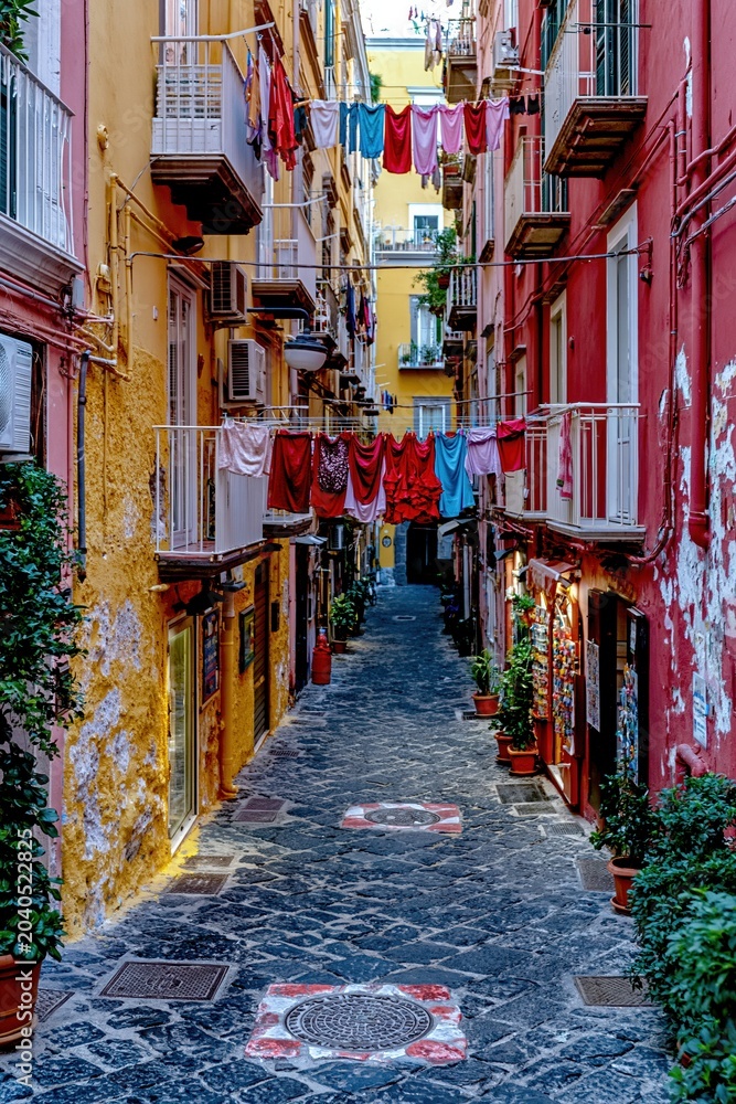 Fototapeta premium Aged colorful apartment buildings lining a narrow cobblestone alley with laundry hanging on lines for travel, urban lifestyle content and Mediterranean street scenery
