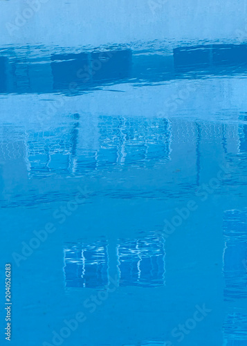 A vibrant, blue image of a building's reflection on a pool's rippling surface.