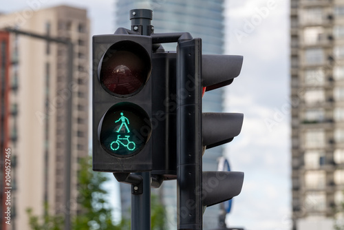 Close-up of a green pedestrian and bicycle crossing signal at an urban intersection with soft blurred buildings in the background.