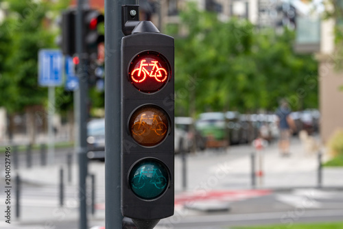 Red bicycle traffic signal at a city crossing with a softly blurred street, trees, and urban background.