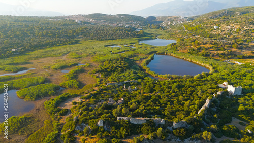 Gelemis, Turkey. Patara Ancient City, weathered stone ruins and crumbling walls rising from dense Mediterranean forest and reed-fringed wetlands, aerial panoramic view at golden hour