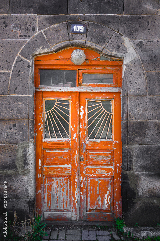 Obraz premium Old rustic door set in stone archway, faded orange with decorative glass
