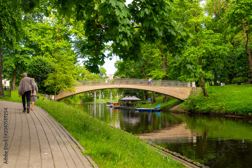 Fotografie people walking along canal path near arched bridge in city park