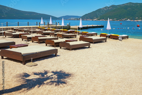 Empty beach. Waiting for summer and resort preparation. Coast of Bay of Kotor with chaise lounges and beach umbrellas. Copy space. Montenegro, Tivat