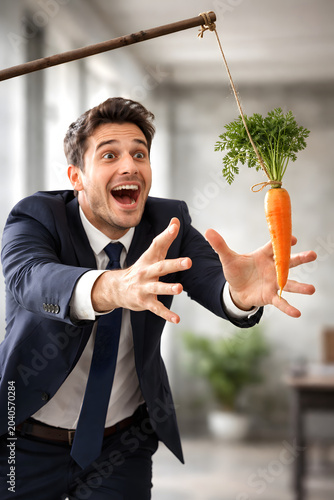 Businessman chasing carrot on a stick, motivation manipulation and unattainable reward concept. Ambitious employee reaching for impossible incentive, workplace productivity pressure, false promises, c
