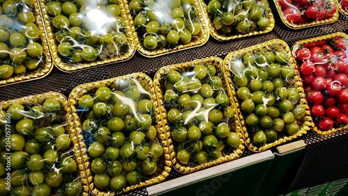 Fresh green olives and red cherry tomatoes arranged in transparent packaging on display at a market, showcasing vibrant colors and appealing presentation for shoppers