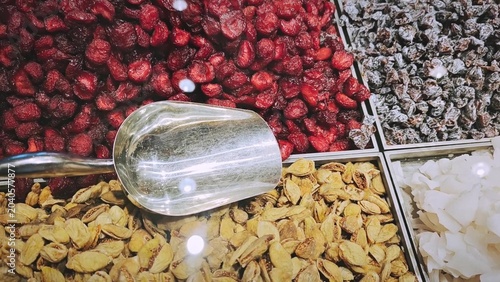 Colorful display of dried fruits and nuts in a market, featuring red raspberries, yellow apricots, green pistachios, and silver scoop for selection