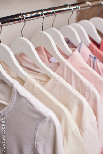 Valokuva Row of various shirts hanging on white hangers on a metal rail inside a closet,