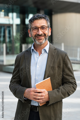 Portrait of confident hispanic professor standing at university school entrance