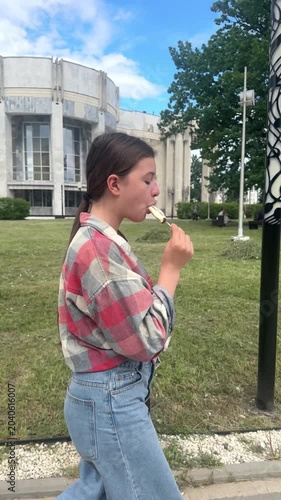 happy child eats ice cream while relaxing in the park on a summer day, girl 13 years old with dark hair eats colorful ice cream, having fun in the amusement park	