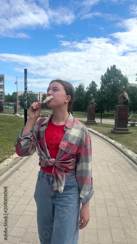 happy child eats ice cream while relaxing in the park on a summer day, girl 11 years old with dark hair eats colorful ice cream, having fun in the amusement park