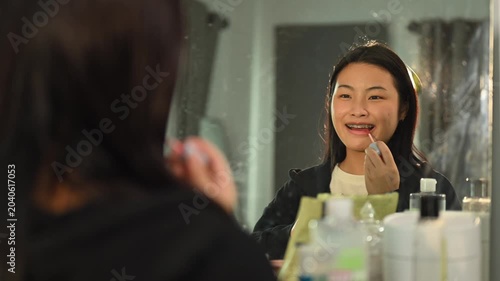 Young Asian Woman Applying Lip Gloss in Bathroom Mirror While Getting Ready for University
