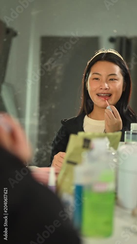 Young Asian Woman Applying Lip Gloss in Bathroom Mirror While Getting Ready for University